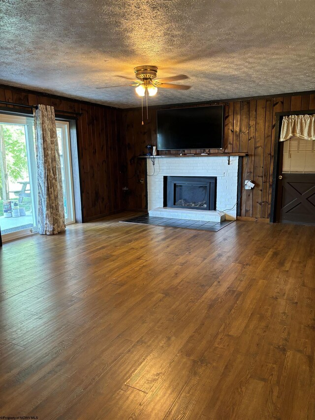 unfurnished living room with ceiling fan, a fireplace, wood-type flooring, and wooden walls