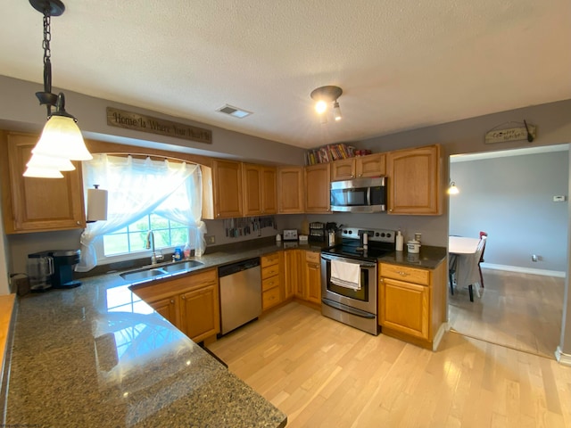 kitchen with a textured ceiling, appliances with stainless steel finishes, decorative light fixtures, light wood-type flooring, and sink