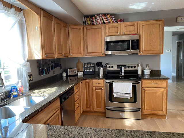 kitchen featuring appliances with stainless steel finishes, dark stone countertops, sink, and light hardwood / wood-style floors