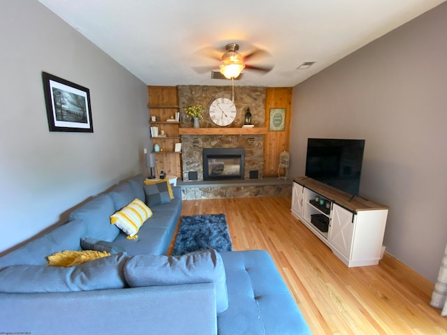 living room featuring ceiling fan, a stone fireplace, and light hardwood / wood-style floors