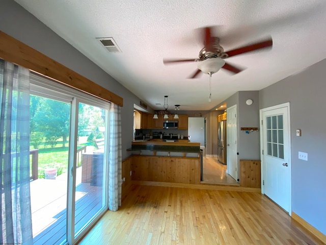 kitchen with appliances with stainless steel finishes, light hardwood / wood-style flooring, a textured ceiling, and ceiling fan