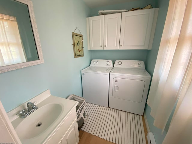 washroom with cabinets, washer and dryer, a baseboard heating unit, sink, and light hardwood / wood-style floors