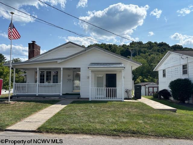 bungalow featuring a front yard, covered porch, and a storage unit