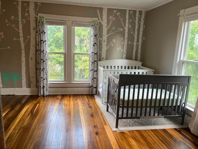 unfurnished bedroom with crown molding, a crib, and hardwood / wood-style flooring