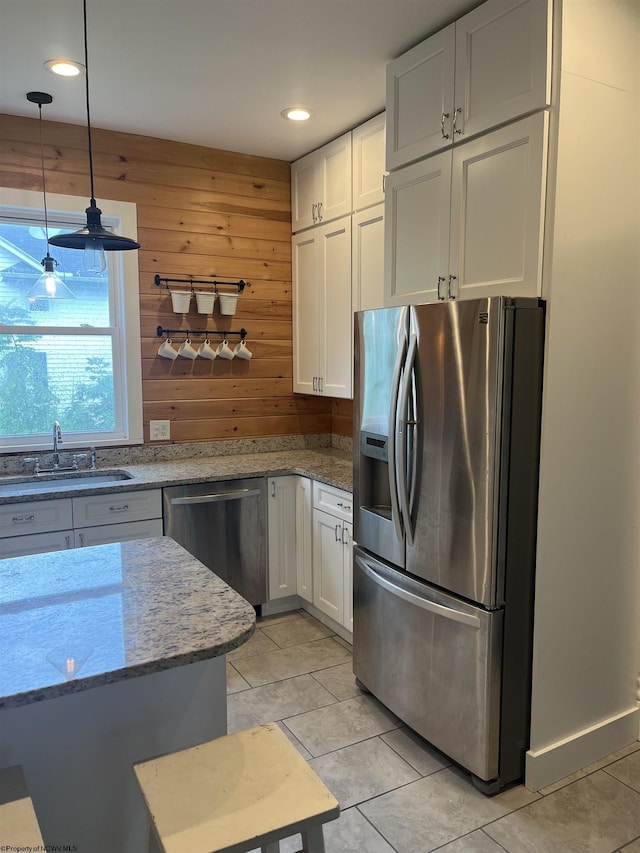 kitchen featuring white cabinetry, wooden walls, stainless steel appliances, and light stone counters