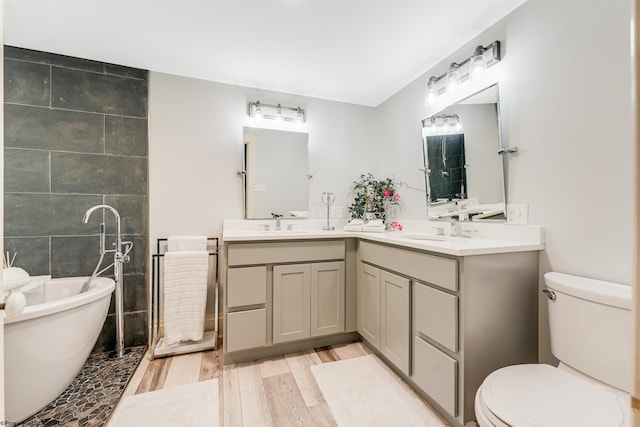 bathroom with toilet, double vanity, a tub to relax in, and wood-type flooring