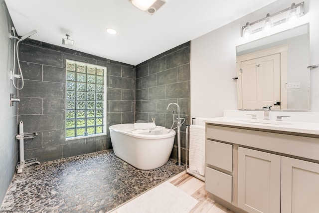 bathroom with hardwood / wood-style floors, a tub to relax in, vanity, and tile walls