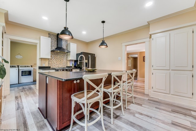 kitchen with backsplash, light hardwood / wood-style flooring, wall chimney exhaust hood, independent washer and dryer, and stainless steel fridge