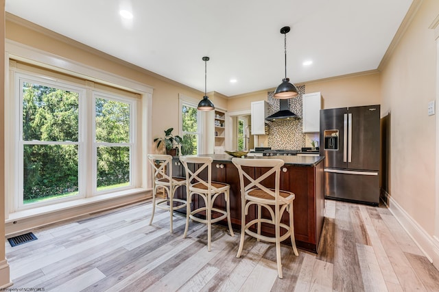 kitchen featuring a wealth of natural light, light wood-type flooring, backsplash, and stainless steel fridge