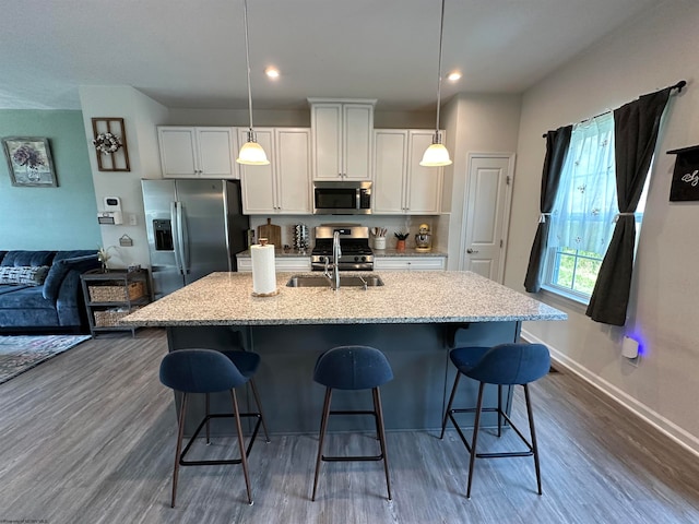 kitchen featuring a breakfast bar, stainless steel appliances, pendant lighting, a center island with sink, and white cabinets