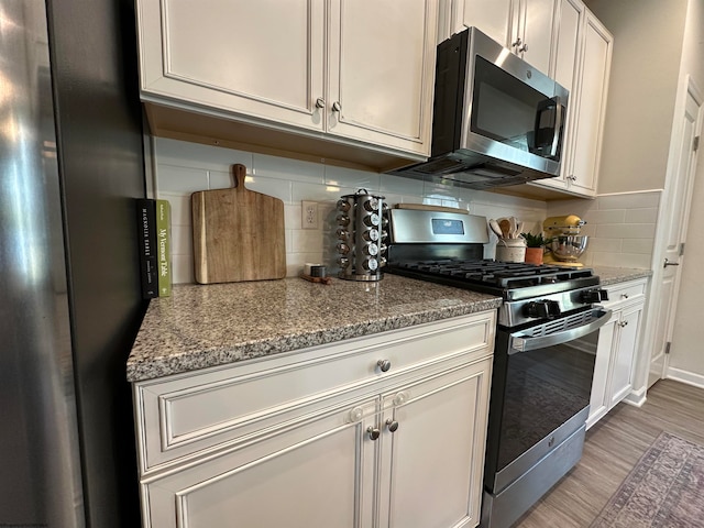 kitchen featuring light stone countertops, tasteful backsplash, stainless steel appliances, light hardwood / wood-style floors, and white cabinetry