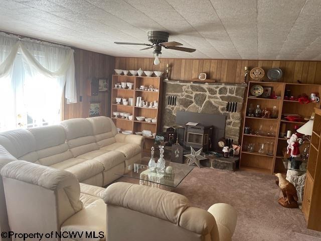 carpeted living room featuring a wood stove, wood walls, and ceiling fan