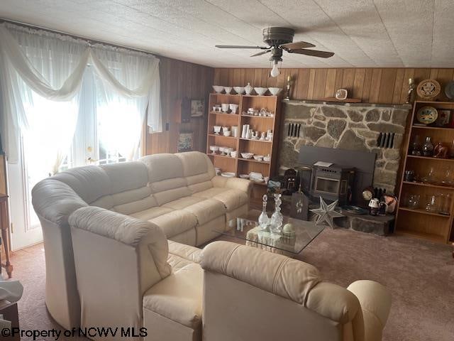 carpeted living room featuring ceiling fan, a wood stove, and wooden walls