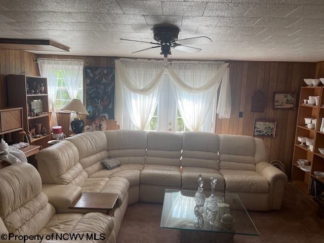 living room featuring a wealth of natural light, carpet, wood walls, and ceiling fan