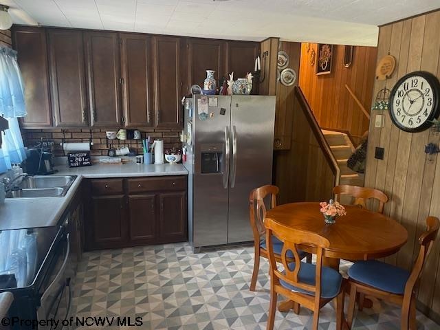 kitchen featuring dark brown cabinetry, sink, stainless steel fridge, wood walls, and range