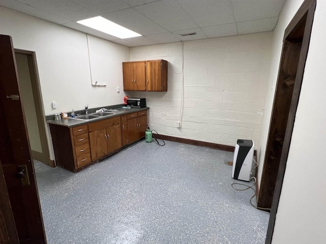 bathroom with concrete block wall, a sink, a drop ceiling, and visible vents