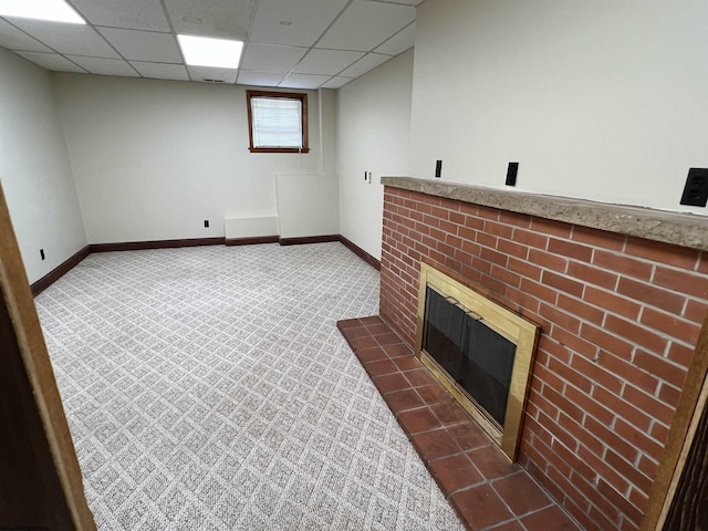 basement featuring baseboards, dark carpet, a drop ceiling, and a brick fireplace