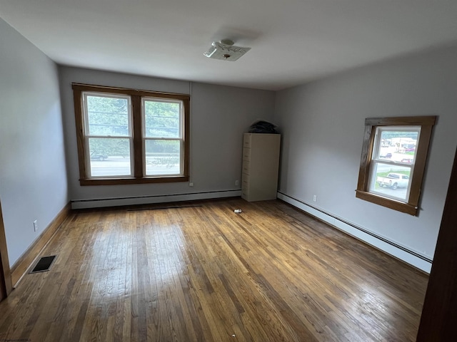 unfurnished room featuring hardwood / wood-style floors, baseboards, visible vents, and a baseboard radiator