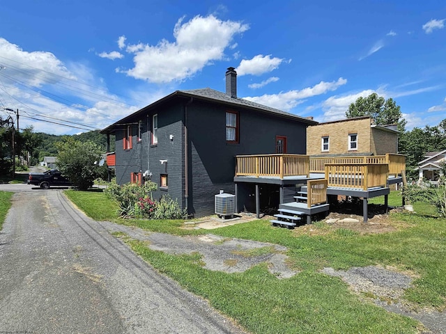 back of house featuring brick siding, a yard, a chimney, a deck, and cooling unit