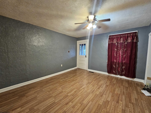 unfurnished room with a textured ceiling, baseboards, wood finished floors, and a textured wall