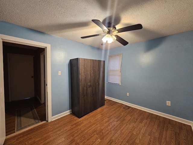 unfurnished bedroom with a ceiling fan, a textured ceiling, baseboards, and wood finished floors
