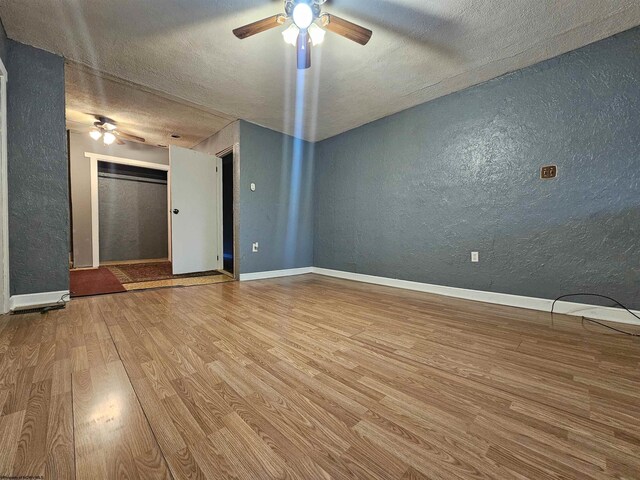 unfurnished living room featuring ceiling fan, light wood-type flooring, and a textured ceiling