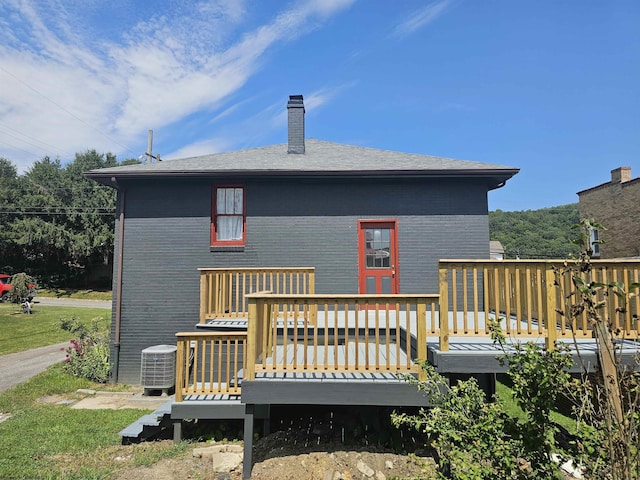 rear view of property featuring brick siding, roof with shingles, a chimney, central AC, and a deck
