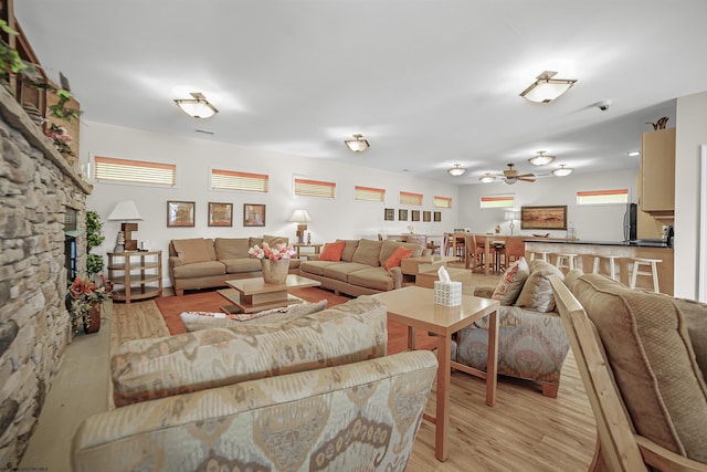 living area featuring light wood-type flooring, ceiling fan, and a stone fireplace