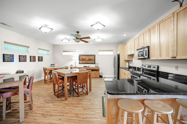 kitchen featuring dark stone counters, appliances with stainless steel finishes, light hardwood / wood-style flooring, light brown cabinets, and ceiling fan