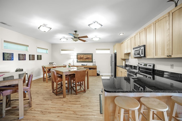 kitchen with visible vents, appliances with stainless steel finishes, a kitchen breakfast bar, dark stone countertops, and light wood-type flooring