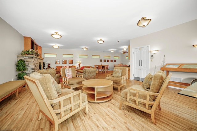 living room featuring ceiling fan, light hardwood / wood-style flooring, and a stone fireplace