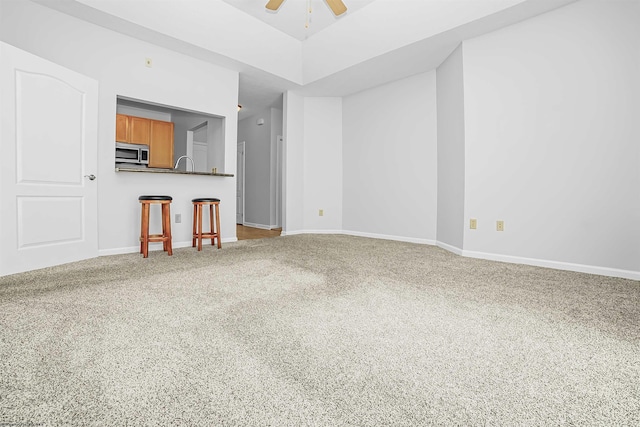 unfurnished living room with carpet floors, baseboards, and a ceiling fan