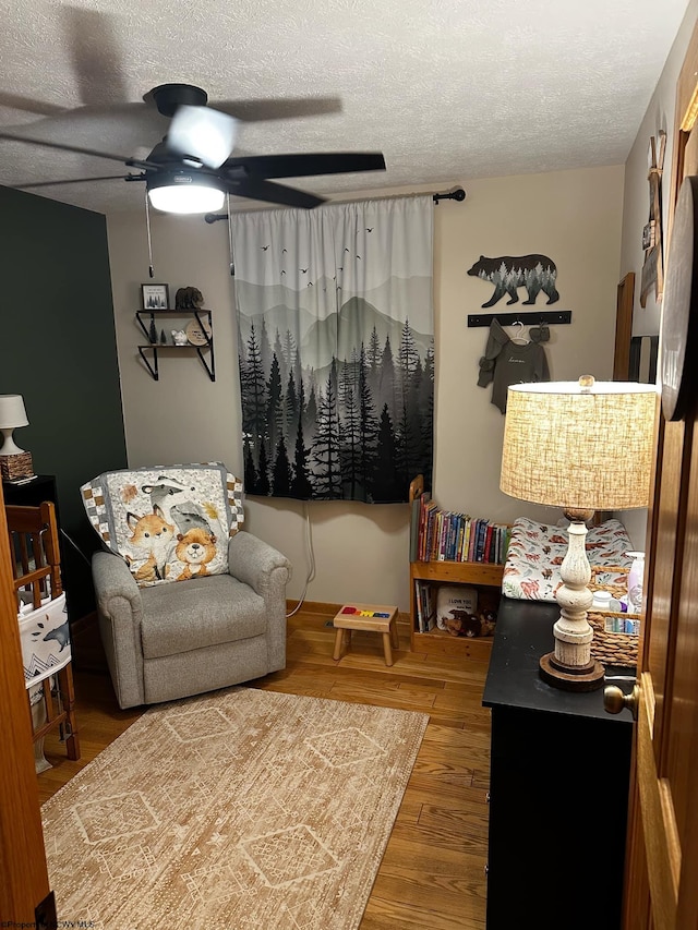 living area with a textured ceiling, a ceiling fan, and wood finished floors