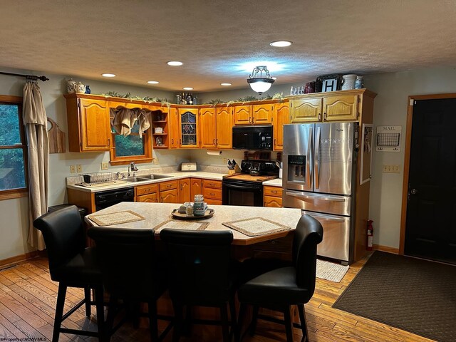 kitchen featuring a kitchen bar, sink, light hardwood / wood-style floors, a textured ceiling, and black appliances