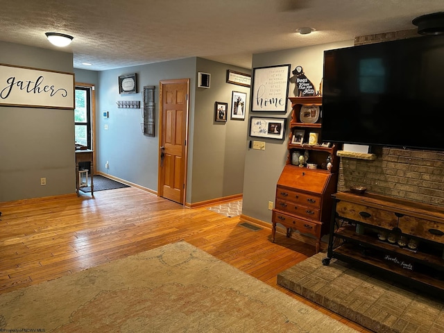 living area with hardwood / wood-style floors, baseboards, visible vents, and a textured ceiling