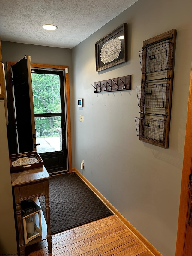 doorway with wood finished floors, baseboards, and a textured ceiling