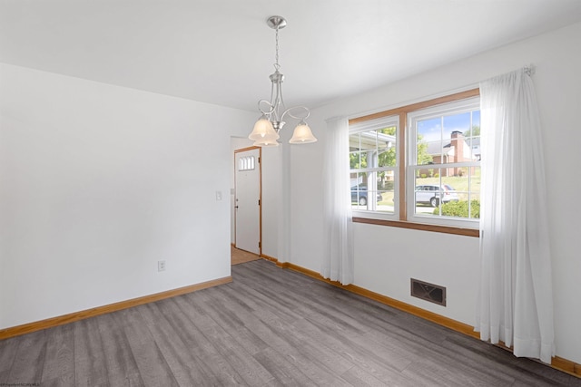 unfurnished room with an inviting chandelier, visible vents, baseboards, and wood finished floors