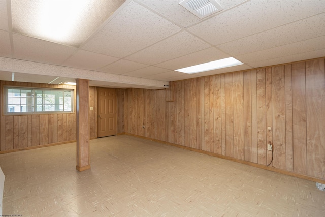 below grade area featuring a paneled ceiling, wooden walls, visible vents, baseboards, and parquet floors