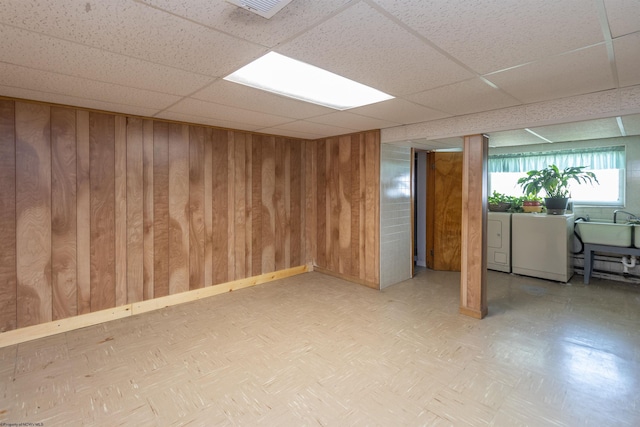 basement featuring a drop ceiling, wood walls, a sink, visible vents, and washing machine and clothes dryer