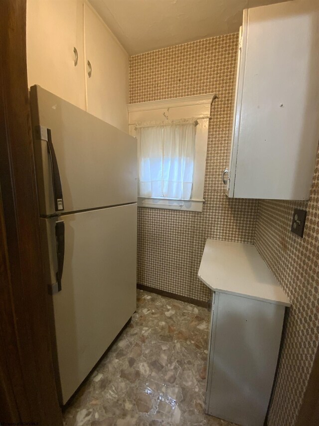 kitchen featuring stainless steel refrigerator, white cabinetry, and tile walls