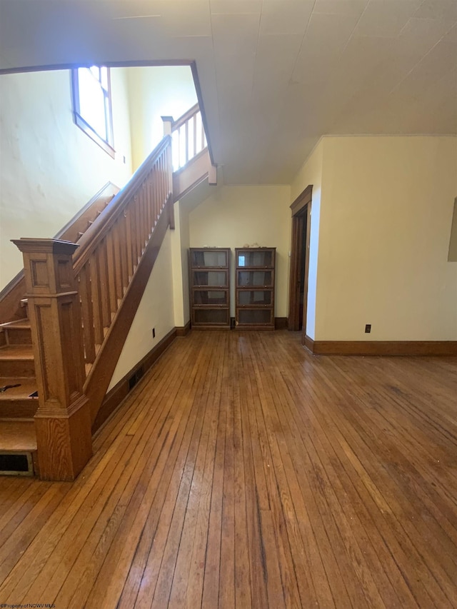 unfurnished living room with stairs, baseboards, and hardwood / wood-style flooring