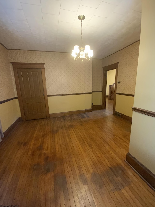 unfurnished room featuring a chandelier, hardwood / wood-style floors, baseboards, and wallpapered walls