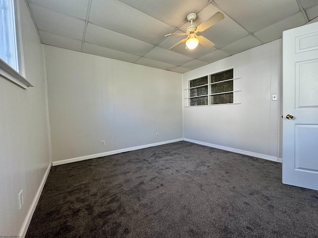 spare room with a paneled ceiling, ceiling fan, baseboards, and dark colored carpet