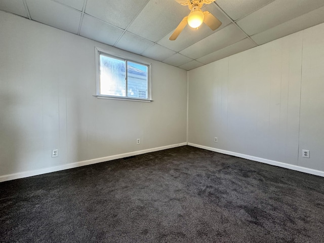 unfurnished room with a ceiling fan, a drop ceiling, dark carpet, and baseboards