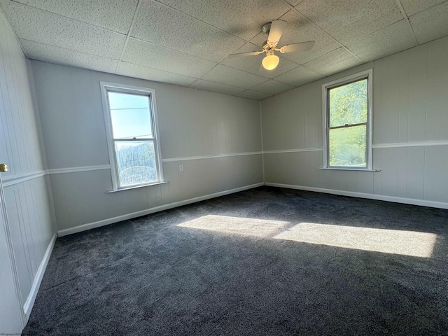 unfurnished room with baseboards, dark carpet, a paneled ceiling, and a ceiling fan