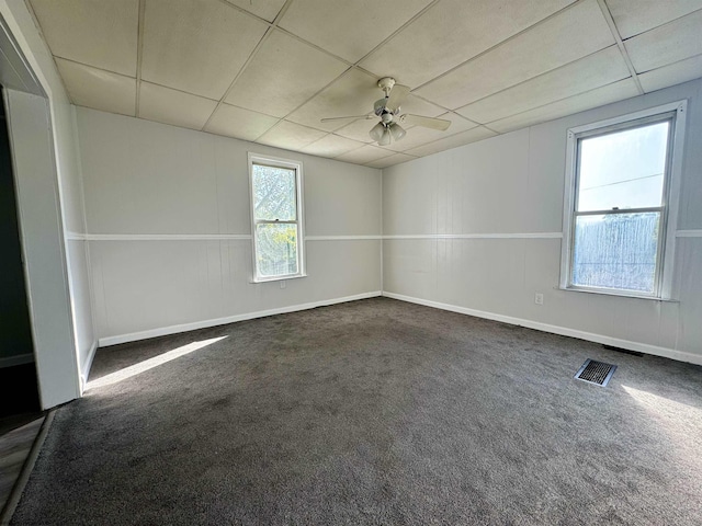 spare room featuring baseboards, visible vents, a ceiling fan, dark colored carpet, and a paneled ceiling