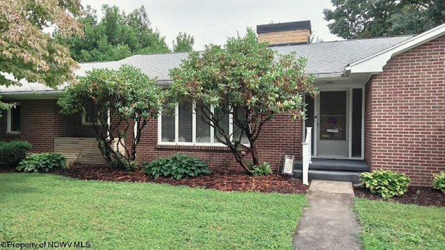 property entrance featuring brick siding, a lawn, a chimney, and a shingled roof