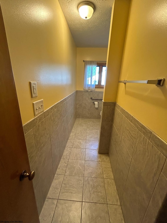 bathroom with a textured ceiling, a wainscoted wall, tile walls, and tile patterned floors