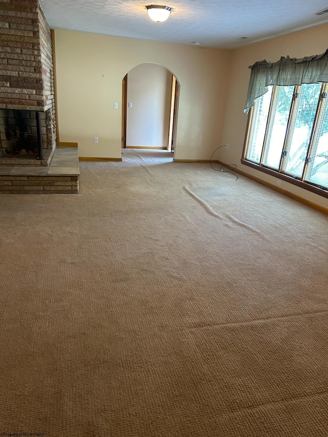 unfurnished living room with light carpet, baseboards, arched walkways, a textured ceiling, and a fireplace