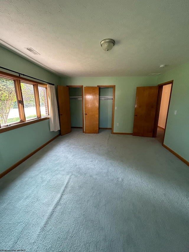 unfurnished bedroom with light colored carpet, visible vents, baseboards, and two closets